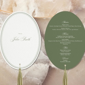 May include: Two oval-shaped menu cards with olive green tassels. The left card is white with a double-line border and the text Welcome Julia Smith. The right card is olive green with white text listing Starters, Mains, Sides, and Dessert.