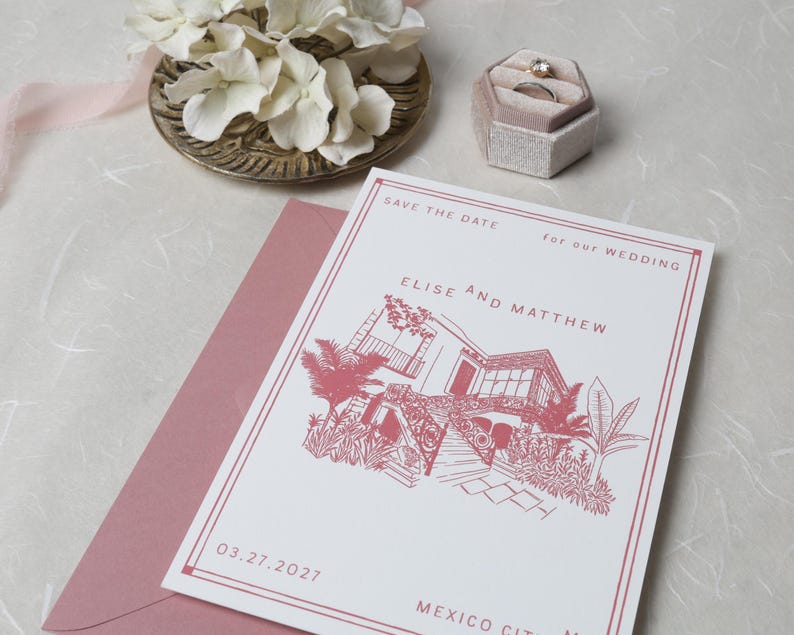 May include: A white save the date wedding card with dusty rose ink featuring a line drawing of a house with palm trees, text reading Elise and Matthew, 03.27.2027, and Mexico City, placed on a dusty rose envelope next to a ring box and white flowers.