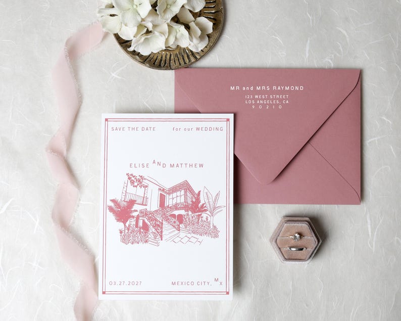 May include: A white save the date card with a pink line drawing of a house, text reading Elise and Matthew, and Mexico City, MX. Accompanied by a dusty pink envelope addressed to Mr and Mrs Raymond, a hexagonal velvet ring box, and a pink ribbon.