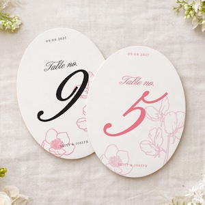 May include: Two oval-shaped table number cards. One card features a black number 9, and the other a pink number 5. Both cards have the text "Table no." and the date "09.08.2027". Floral illustrations and the names "SALLY & JOSEPH" are also present.
