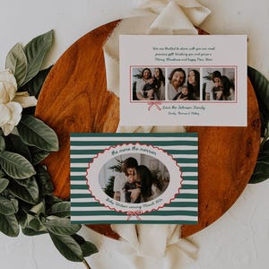 Op de afbeelding: Twee kerstkaarten met familiefoto's. Eén heeft een groen-wit gestreept ontwerp met de tekst "the more the merrier". De andere kaart toont een reeks familiefoto's. Ze liggen op een houten oppervlak met bladeren en bloemen.