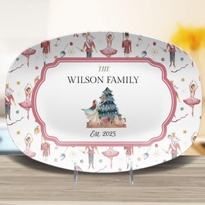 May include: An oval decorative plate with a pink and white design featuring ballet dancers, toy soldiers, and a Christmas tree. The center of the plate has the text "THE WILSON FAMILY" and "Est. 2025".