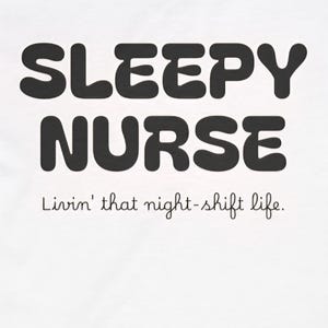 以下が含まれることがあります： 大きな黒い丸みを帯びた文字で「SLEEPY NURSE」と書かれた白いVネックTシャツ。テキストの下には、手書き風のフォントで「Livin' that night-shift life」というフレーズがあります。シャツの首元にはタグが付いています。