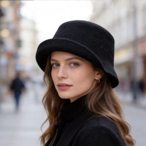 Può includere: Un cappello a secchiello in feltro nero tinta unita con corona arrotondata e tesa leggermente rivolta verso il basso. Il cappello presenta una consistenza liscia e uniforme e un colore scuro profondo, creando una silhouette classica.