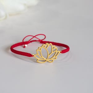 May include: A red cord bracelet featuring a gold-colored lotus flower charm. The bracelet is adjustable with a sliding knot closure. The lotus flower is a symbol of purity, enlightenment, self-regeneration and rebirth.