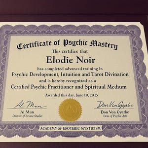 Op de afbeelding: Ingelijst certificaat van Psychic Mastery, toegekend aan Elodie Noir. Het certificaat, met een decoratieve rand, erkent een gevorderde opleiding in psychische ontwikkeling, intu&iuml;tie en tarotdivinatie. Ondertekend door Al Mun en Don Von Gyurke, gedateerd 10 juni 2015.