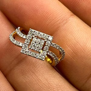 Puede incluir: Un anillo de oro con un centro cuadrado con diamantes y un dise&ntilde;o de doble banda. El anillo presenta un patr&oacute;n geom&eacute;trico con numerosos diamantes peque&ntilde;os y brillantes, creando una apariencia lujosa y elegante. El anillo se muestra en primer plano.