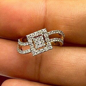 Puede incluir: Un anillo de oro con un centro de racimo de diamantes cuadrados y diamantes m&aacute;s peque&ntilde;os a lo largo de la banda. El dise&ntilde;o del anillo presenta un estilo de doble banda con un patr&oacute;n geom&eacute;trico calado, que muestra el brillo de las piedras preciosas.