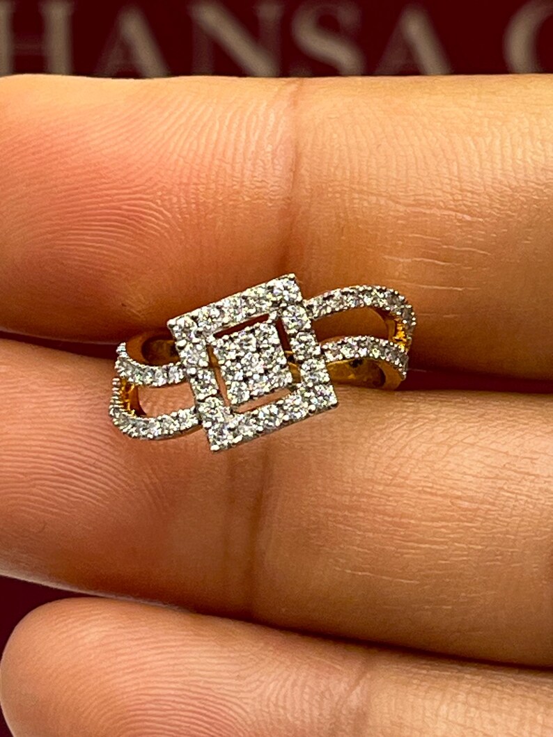 Puede incluir: Un anillo de oro con un centro de racimo de diamantes cuadrados y diamantes m&aacute;s peque&ntilde;os a lo largo de la banda. El dise&ntilde;o del anillo presenta un estilo de doble banda con un patr&oacute;n geom&eacute;trico calado, que muestra el brillo de las piedras preciosas.