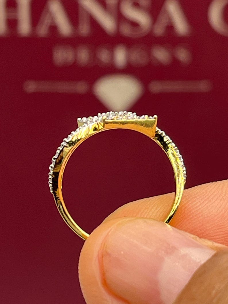 Puede incluir: Primer plano de un anillo de oro con un grupo de diamantes cuadrados y diamantes m&aacute;s peque&ntilde;os a lo largo de la banda. El anillo se sostiene sobre un fondo rojo, mostrando los detalles de la joya.