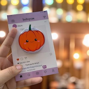 May include: A cute orange pumpkin-shaped phone grip with a smiling face, attached to a card designed to look like an Instagram post. The card has the Instagram logo and a caption that says "Thank you for liking it."