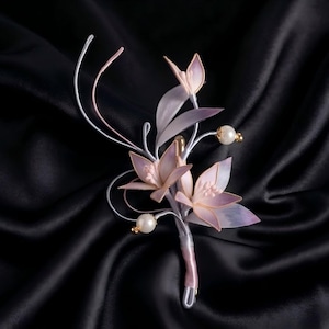 May include: A floral brooch featuring three delicate, translucent pink and white petals arranged on silver-toned wire stems. The design includes two small white spherical beads and long, curved wire accents, all secured with a wrapped stem base.
