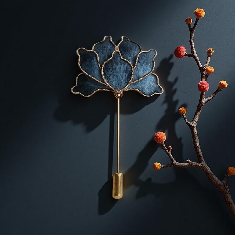 May include: A decorative wall hanging in the shape of a blue lotus flower with gold trim and a long gold stem. The flower is mounted on a dark blue wall, with a branch of orange and yellow buds to the right.