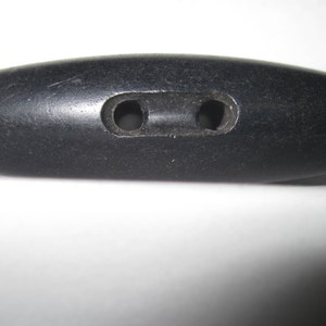 May include: A black wooden button with two holes. The button is oval shaped and has a smooth surface.