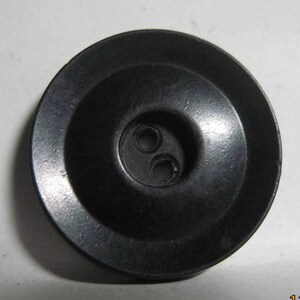 May include: A black plastic button with two holes. The button has a raised center and a flat, smooth surface.
