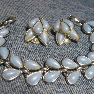 May include: A set of light blue teardrop-shaped earrings and a matching bracelet. The jewelry is made of silver-toned metal and features a cluster of teardrop-shaped stones.
