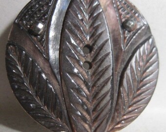 May include: A dark brown, round, carved button with a leaf design. The button has two holes and a shiny, metallic finish.