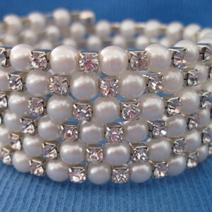 May include: A white pearl and rhinestone bracelet with multiple rows of pearls and rhinestones.