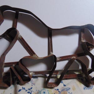 May include: A rusty metal cookie cutter shaped like a horse. The cutter is made of thin metal and has a simple design.