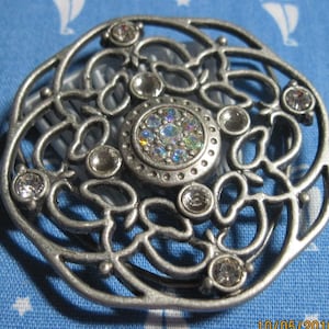 May include: Silver hair comb with a decorative design featuring a large central rhinestone cluster and smaller rhinestones around the perimeter.