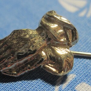 May include: A silver-toned praying hands pin with a detailed design. The pin is attached to a thin silver-toned rod.