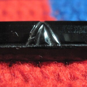 May include: A black, rectangular, carved obsidian stone with a pointed top.