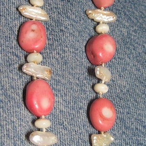 May include: A pink and white beaded necklace with large, oval-shaped pink beads and smaller, round white beads. The necklace is strung on a thin white cord.