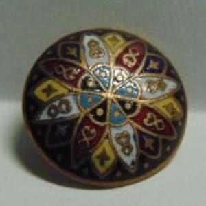 May include: A round, decorative button with a floral design. The button features a dark brown background with a gold rim and a colorful flower pattern in red, yellow, blue, and white. The button is approximately 1 inch in diameter.