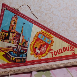 May include: A red, white, and blue triangular pennant with a picture of a church and fountain on one side and a coat of arms with the word "TOULOUSE" on the other side.