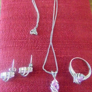 May include: A silver necklace, ring, and earrings set with pink gemstone accents. The necklace features a pendant with a pink gemstone in a marquise shape.