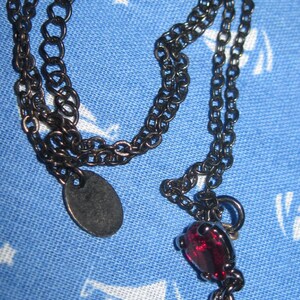 May include: A black chain necklace with a teardrop-shaped pendant featuring two red gemstones.