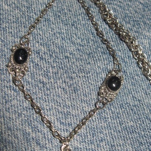 May include: A silver chain necklace with three black gemstone pendants. The necklace has a delicate, intricate design.