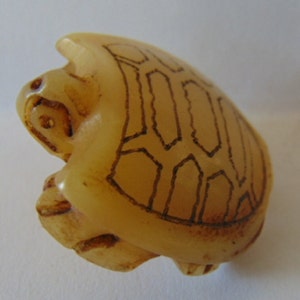 May include: A small, carved turtle figurine made of light brown stone. The turtle's shell has a detailed etched pattern.