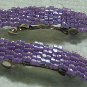 May include: Two purple beaded hair clips with silver metal clasps. The clips are made of small, square beads that are arranged in rows.