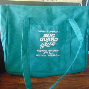 May include: A teal blue tote bag with white embroidered text that reads "SKIN-SO-SOFT BUG GUARD plus Help Keep Your Family BITE-free DEET-free WORRY-free"