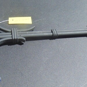 May include: A dark gray metal hanging bracket with a hook end. The bracket has a flat mounting plate and a horizontal arm with decorative details. A yellow tag is attached with white string.