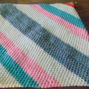 May include: A crocheted baby blanket with diagonal stripes in white, pink, teal, gray, and orange.