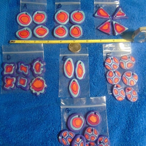 May include: Six bags of colorful, handmade polymer clay earrings. The earrings are in various shapes and designs, including circles, ovals, and abstract shapes. The colors are predominantly blue, orange, and red.