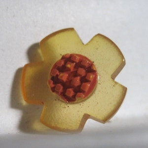 May include: A yellow plastic flower with a red center. The center is made of a grid of small squares.