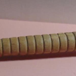 May include: A vintage wooden spindle, likely for textile work. The spindle is light brown with a series of evenly spaced grooves along its length. The end has a wider, rounded head with metal accents. The overall design suggests a tool for spinning or winding thread.