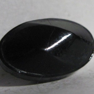 May include: A black, oval-shaped button with a raised, pointed center.