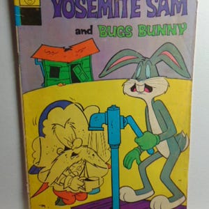 May include: A vintage comic book featuring Yosemite Sam and Bugs Bunny. The cover has a purple background with the title in large, stylized letters. Bugs Bunny stands near a blue water pump, while Yosemite Sam is being splashed with water. The comic is yellowed with age.