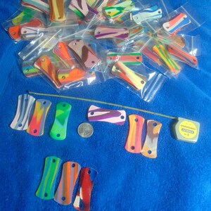 May include: A collection of colorful, handmade, plastic, rectangular, patterned, keychains with holes for attaching to a key ring. The keychains are in various colors, including red, blue, green, yellow, and purple.