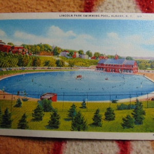 May include: A vintage postcard depicting a swimming pool with a building in the background. The postcard reads "Lincoln Park Swimming Pool, Albany, N.Y. 103".