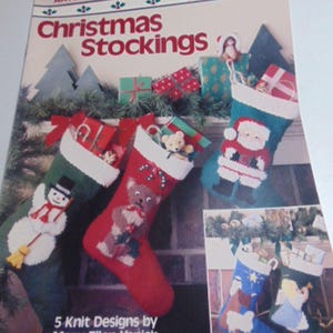 May include: A Leisure Arts craft leaflet titled Christmas Stockings featuring five knit designs by Mary Ellen Yanich. The cover displays three stockings with snowman, teddy bear, and Santa motifs, plus two smaller images of nativity stockings.