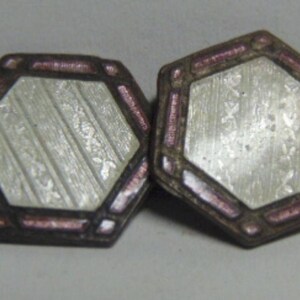 May include: A pair of vintage cufflinks. Each cufflink has a hexagonal shape with a silver-colored center and a dark brown border with pink accents. The center has a textured, striped design.