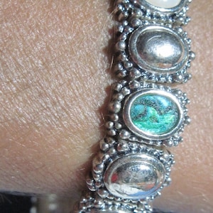 May include: A silver bracelet with a series of oval-shaped charms. The charms are decorated with white, green, and black stones.