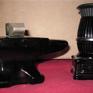 May include: Two black glass figurines. One is shaped like an anvil and the other is shaped like a wood-burning stove. Both have a shiny, polished finish.