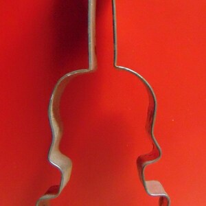 May include: A metal cookie cutter shaped like a violin. The cutter is made of a single piece of metal and has a smooth, shiny finish.