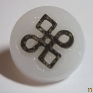 May include: White button with a black and gray intricate design. The design is a stylized knot or symbol.